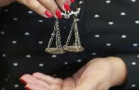 Fotografia da imagem de uma mão feminina, segurando o símbolo da balança do equilíbrio da justiça.