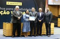 #ParaTodosVerem: Fotografia colorida. Na imagem, estão cinco pessoas de pé, uma mulher e quatro homens, todos sorriem para a fot