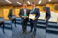 Fotografia em ambiente fechado que reúne dois homens pardos, lado a lado, segurando premiações do CSJT
