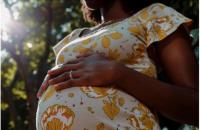 Mulher gestante com vestido florido branco e amarelo, com a mão acima da barriga