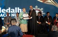 Foto em ambiente fechado mostrando a cerimonia solene de entrega da  Medalha da Ordem de Mérito de Contas “Governador Alacid"