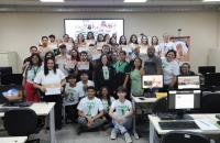 #ParaTodosVerem: Fotografia colorida em ambiente fechado reunindo homens e mulheres, todos estão em pé sorrindo para a foto.