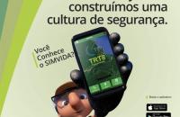 Mascoto do TRT8 segurando um celular com a imagem do aplicativo SIMVIDA