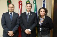 tres pessoas em pé em frente as bandeira posicionados pra foto