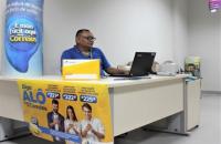 Na foto: Servidor dos Correios mexendo no notebook, na frente uma caixa de envio e um banner divulgando um serviço dos correios.