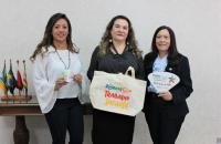 Foto:   juíza, presidente e desembargadora posam com as peças nas mãos.