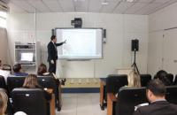 Foto: coordenador de gestão estratégica explicando os dados em frente a lousa onde são projetados os slides.