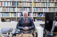 senhor desembargador sentado na frente de sua estante de livros