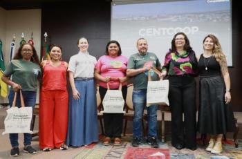 Fotografia em ambiente fechado que reúne sete pessoas em pé, lado a lado, entre homens e mulheres.
