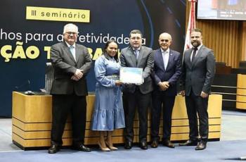 #ParaTodosVerem: Fotografia colorida. Na imagem, estão cinco pessoas de pé, uma mulher e quatro homens, todos sorriem para a fot