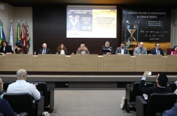 Foto dos participantes da mesa da abertura posicionados para o início da mesa. Mais a frente, o público sentado também aguarda.