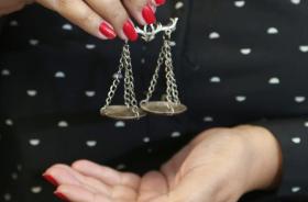 Fotografia da imagem de uma mão feminina, segurando o símbolo da balança do equilíbrio da justiça.