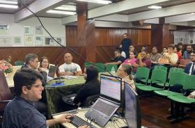 Foto colorida do auditório da Unama durante a audiência, com diversos alunos na plateia.