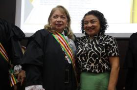 Fotografia em ambiente fechado que reúne duas mulheres sorrindo.