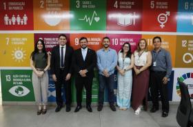 #ParaTodosVerem: Fotografia colorida em ambiente fechada, na foto está presente todos os participantes da reunião, em pé e sorri